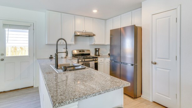 A modern kitchen with white cabinetry, a granite countertop, stainless steel appliances, and a large refrigerator. - 7 Mi to Alamo Ranch Mall: Home w/ Large Yard! (San Antonio)