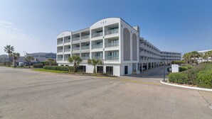 A multi-story hotel with a white facade, balconies, and a parking area. - Walk to Galveston Fishing Pier: Condo w/ Balcony (Galveston)