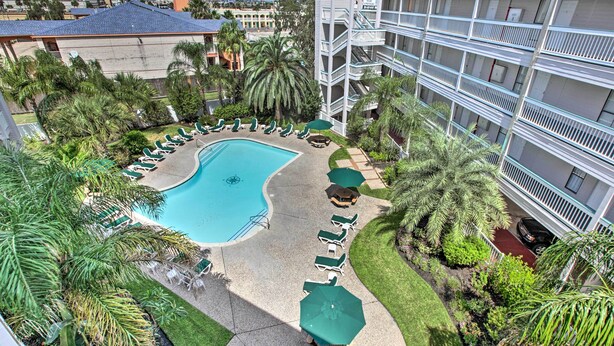 A pool area with lounge chairs and umbrellas, surrounded by palm trees and a building with balconies. - Walk to Galveston Fishing Pier: Condo w/ Balcony (Galveston)