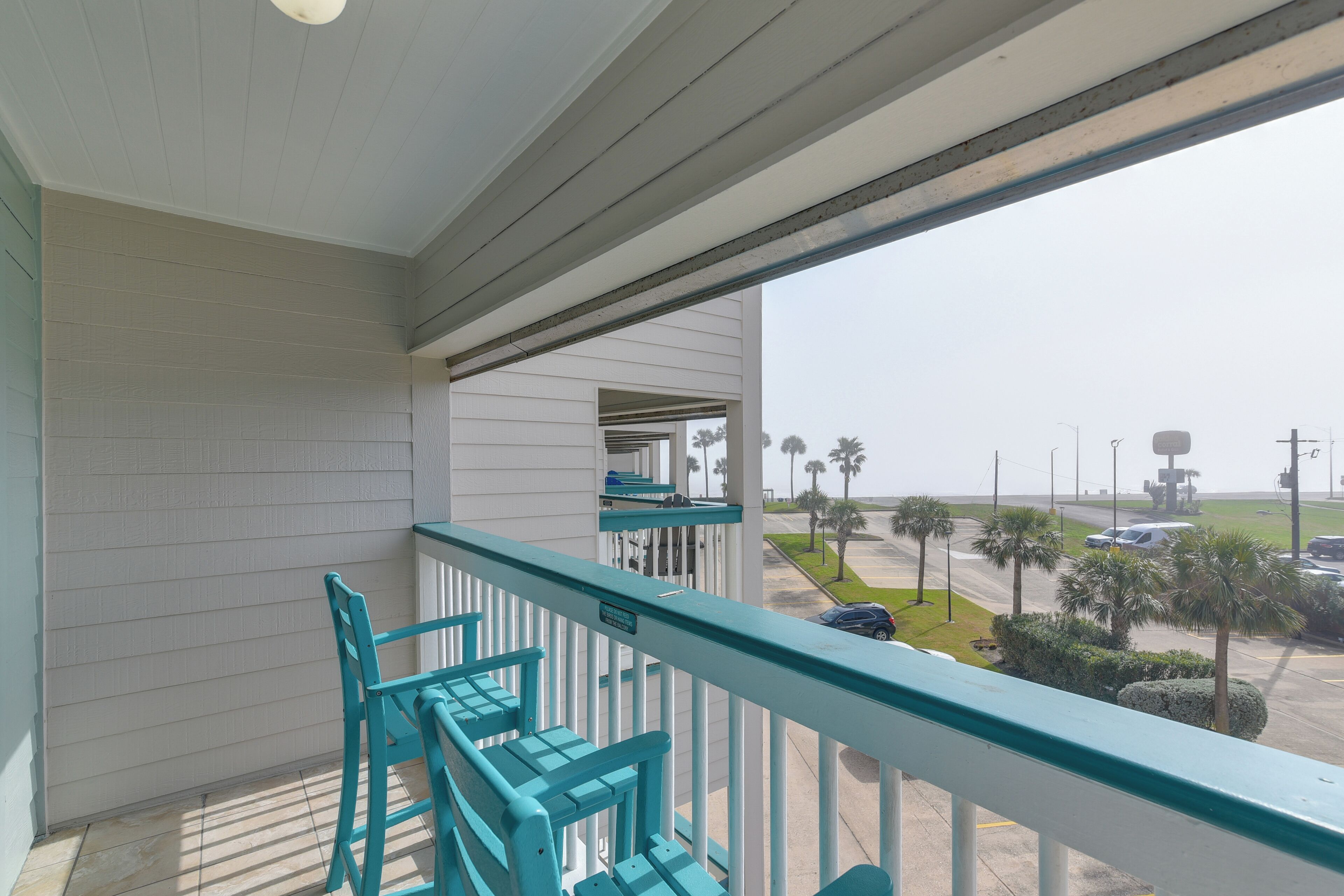 A balcony with a view of a parking lot and palm trees.