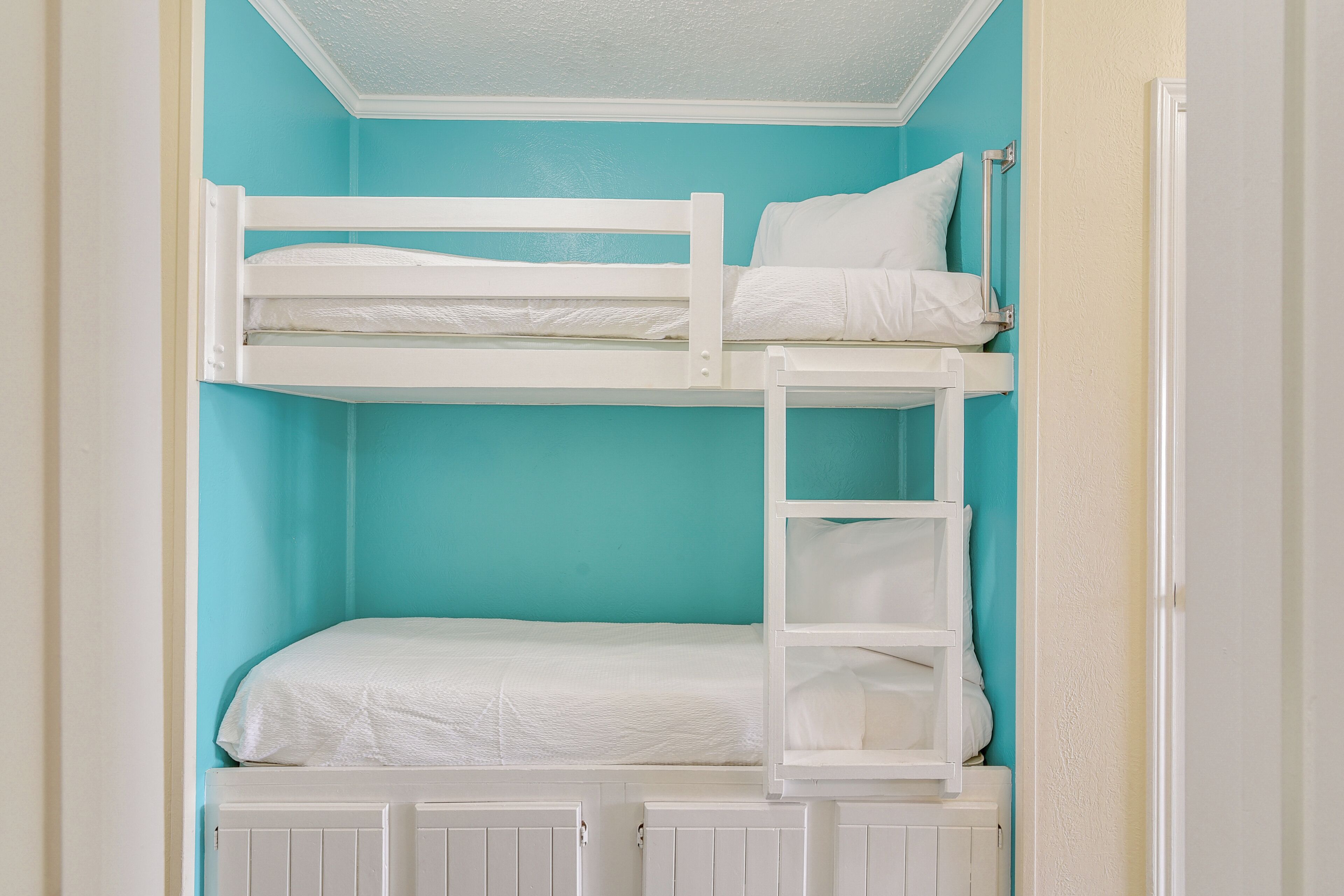 A bunk bed with white bedding and a ladder, set against a teal wall.