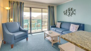 A room with a blue armchair, a sofa, a small table, and a large window with curtains. - Walk to Galveston Fishing Pier: Condo w/ Balcony (Galveston)