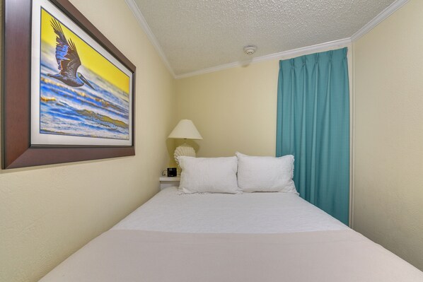 A hotel room with a bed, a painting of a bird, a lamp, and a window with curtains.