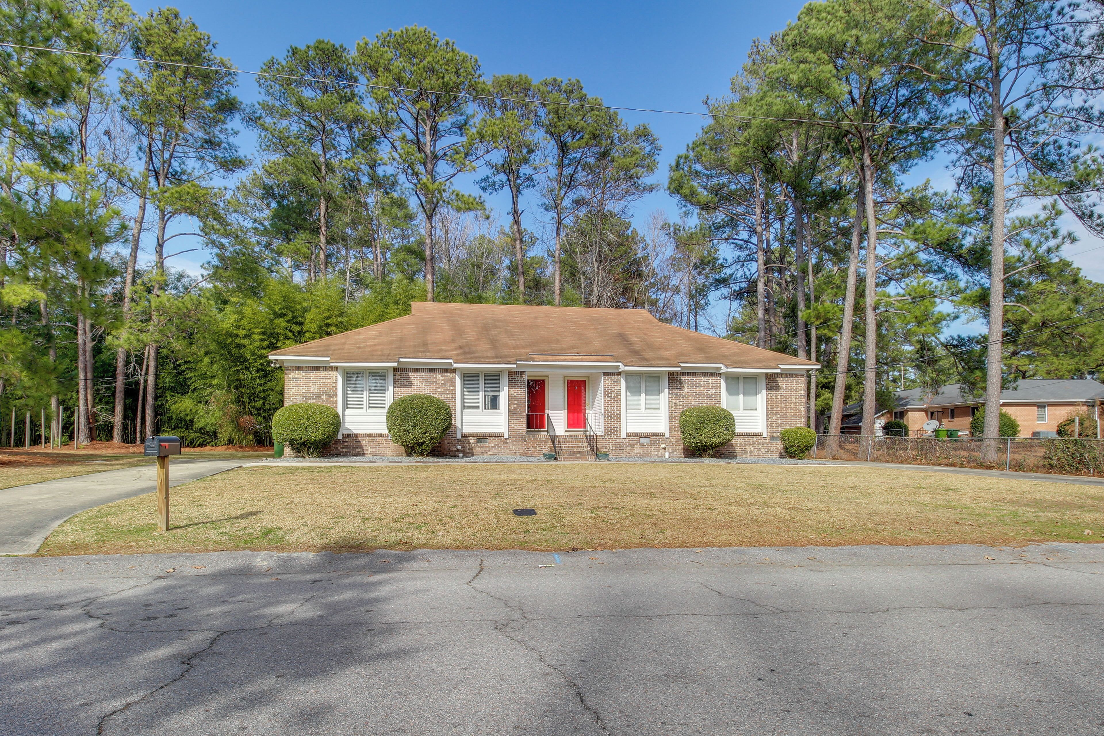 A two-story house with a red front door, a brick facade, and a small front yard.