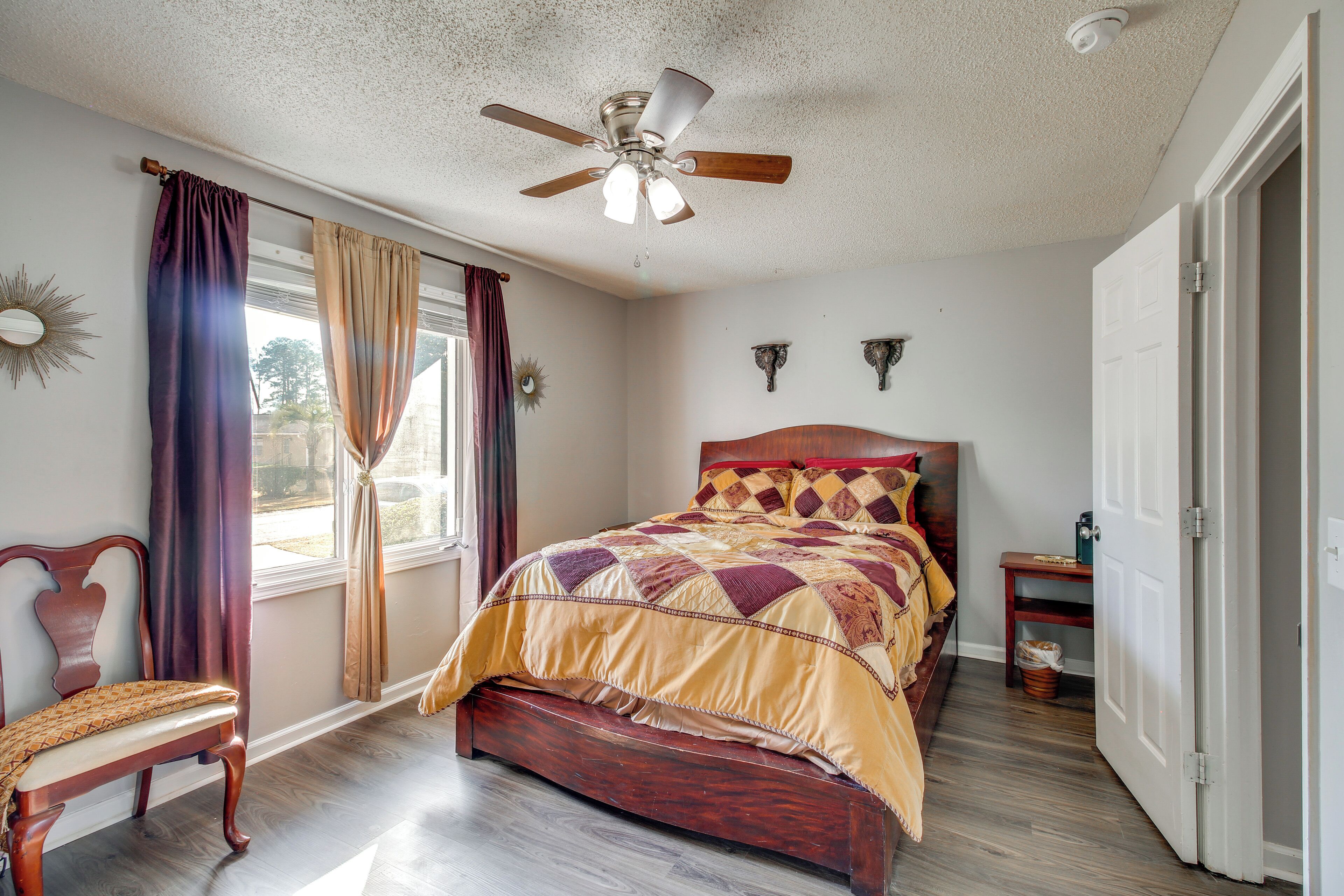 A bedroom with a wooden bed, a ceiling fan, a window with curtains, and a nightstand.
