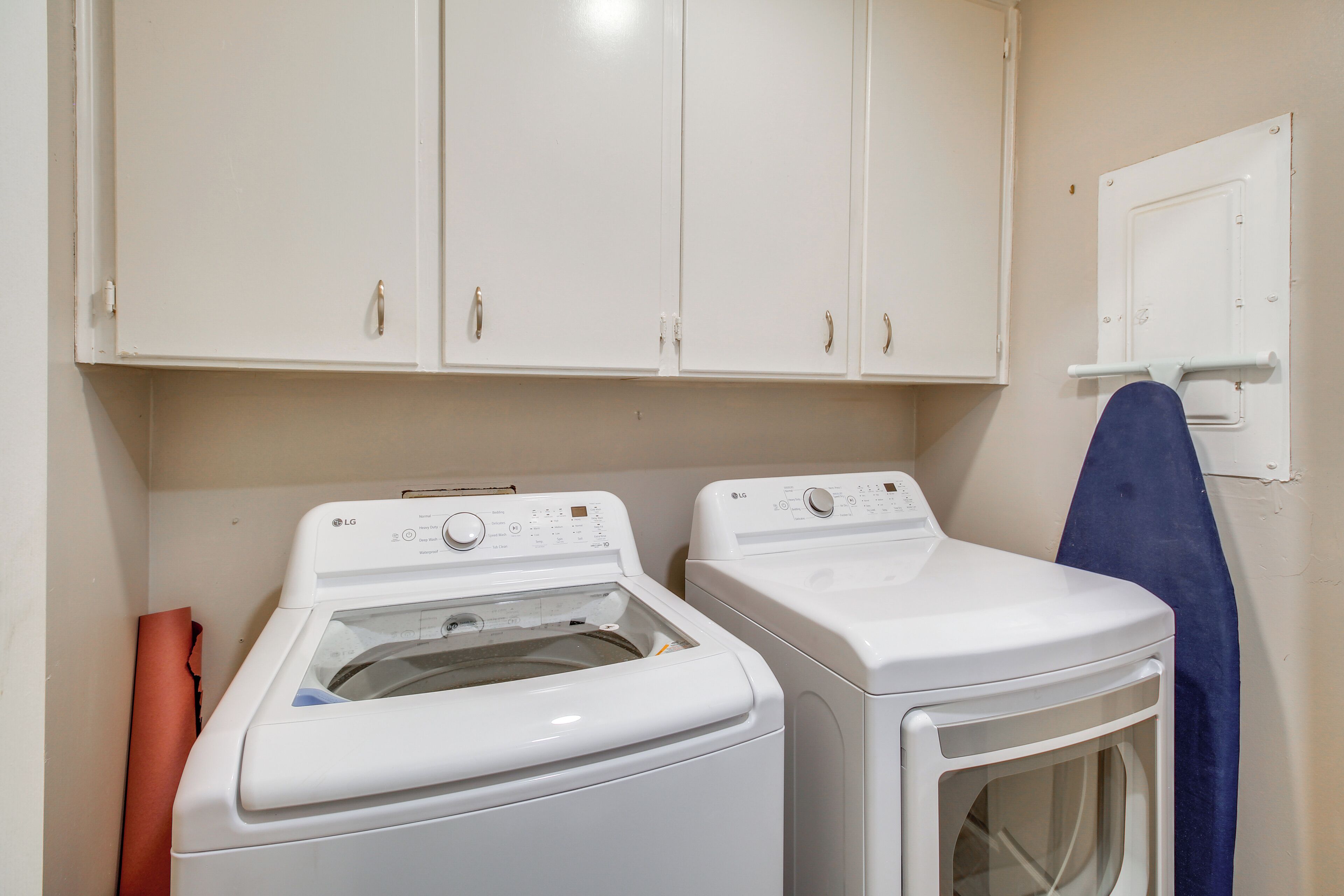 A laundry area with two white washing machines, a blue towel hanging on a rack, and white cabinets above.