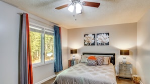 A bedroom with a bed, curtains, a ceiling fan, a nightstand with a lamp, and wall art. - Easy Access to I-77 & I-20: Columbia Duplex! (Columbia)