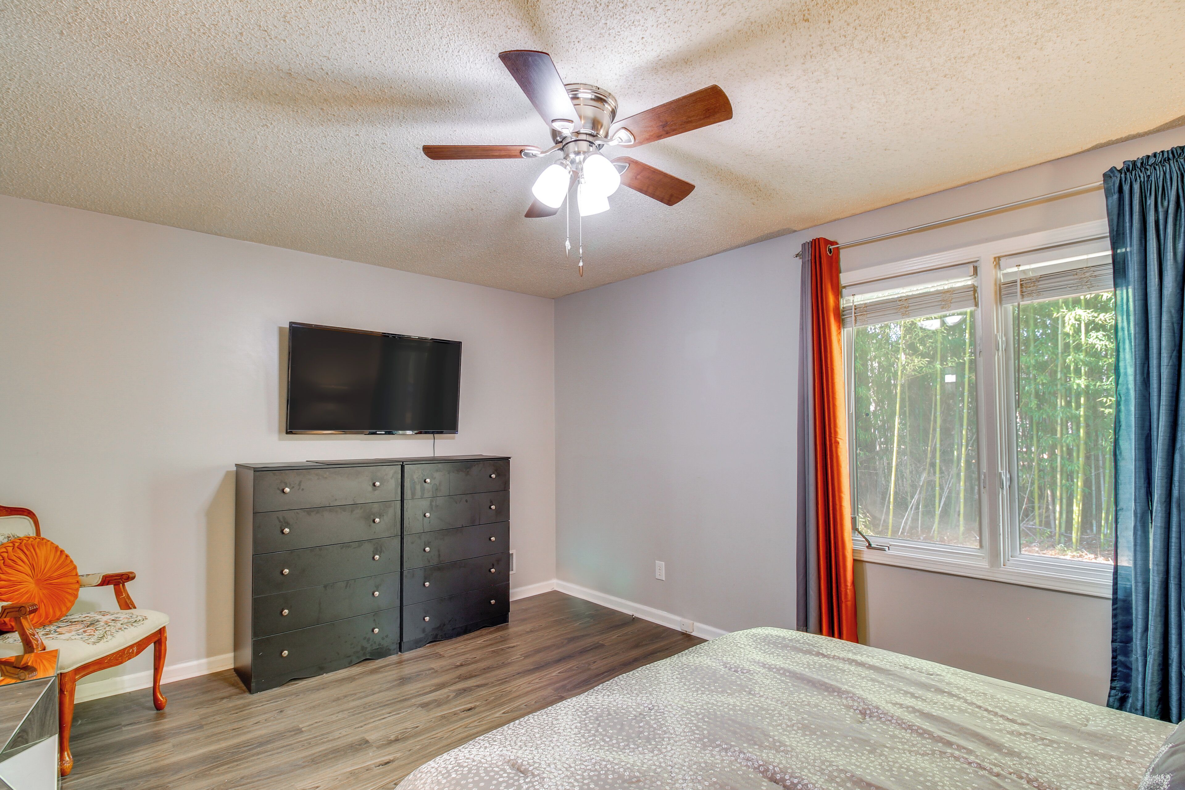 A bedroom with a ceiling fan, a dresser, a bed, a TV, and a window with curtains.