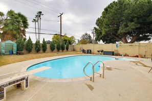 A swimming pool with a tiled deck and metal ladder, surrounded by a brick wall, palm trees, and a large tree. - 10 Mi to Redondo Beach: Carson Home w/ Pool Table! (Carson)