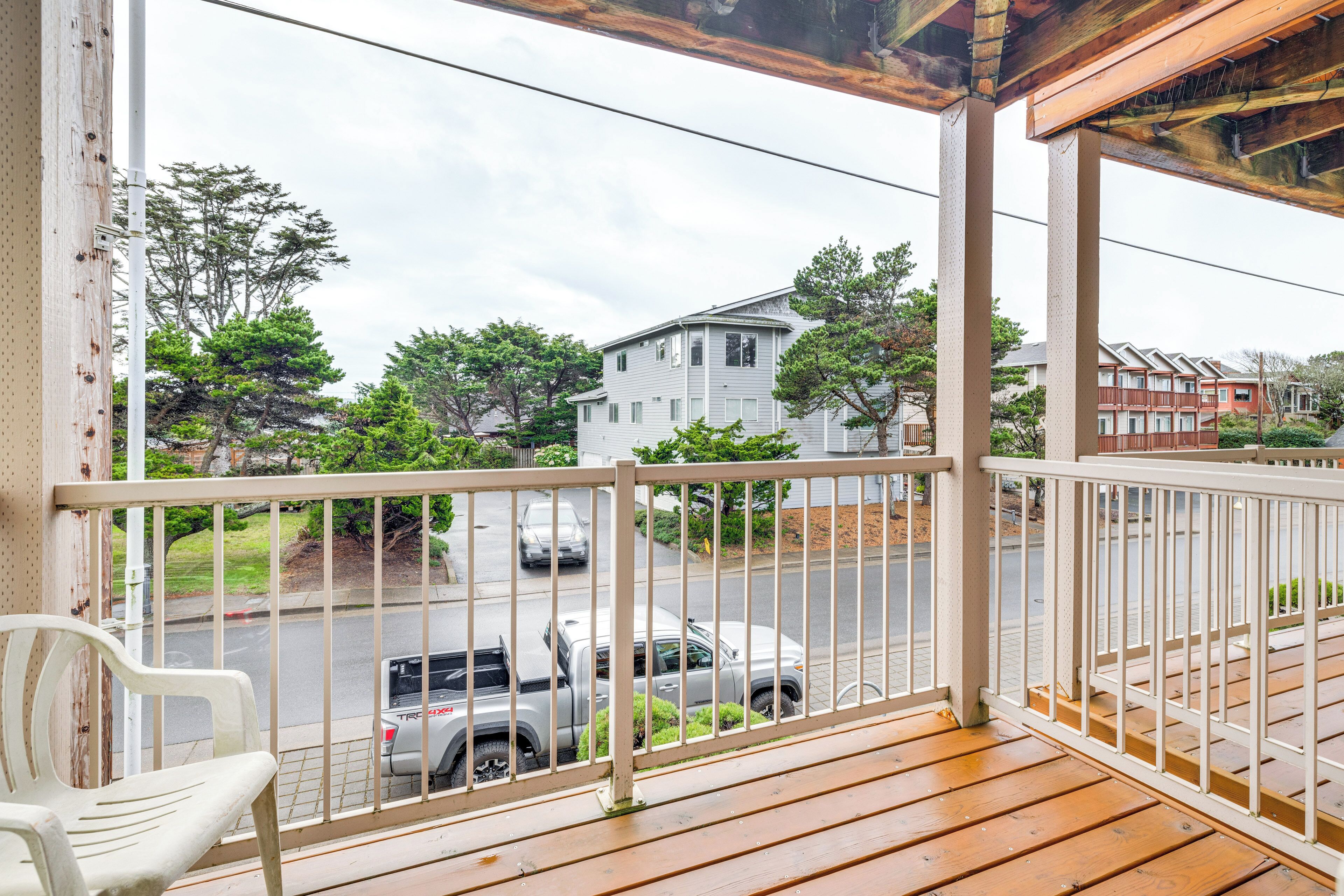 A wooden deck with a white railing, overlooking a street with parked cars and houses.