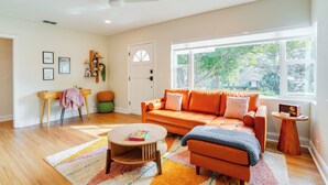 A modern living room with a large window, a ceiling fan, and a wooden coffee table. - Mid-century Lakeland Home w/ Game Room! (Lakeland)