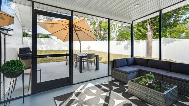 An outdoor patio area with a dining table, chairs, a sofa, and a large umbrella. - Mid-century Lakeland Home w/ Game Room! (Lakeland)