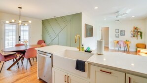 A modern kitchen with a central island, white cabinetry, and a dining area with pink chairs. - Mid-century Lakeland Home w/ Game Room! (Lakeland)