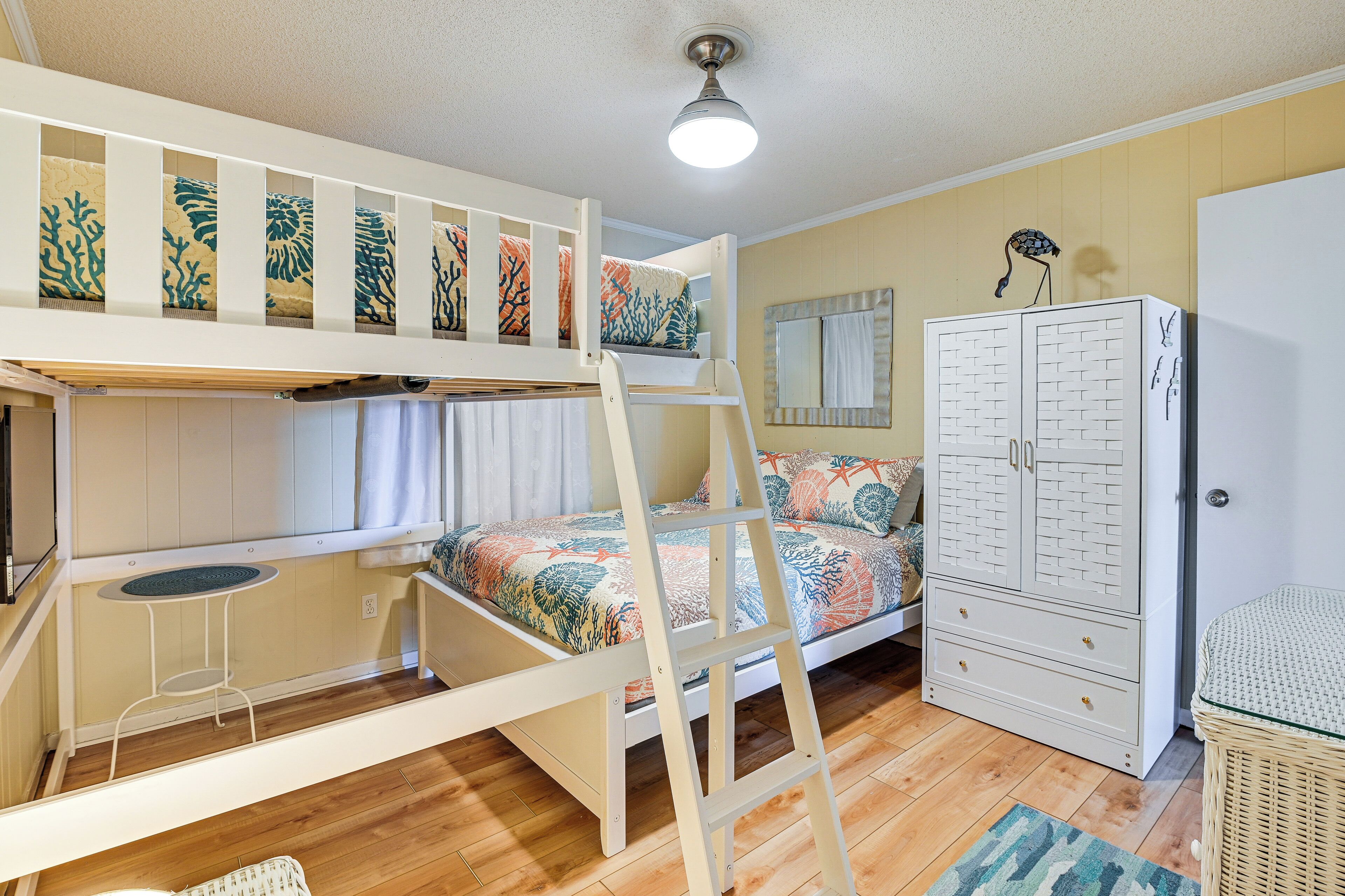 A bunk bed with a ladder, a small table, a wardrobe, and a mirror.