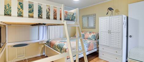 A bunk bed with a ladder, a small table, a wardrobe, and a mirror.