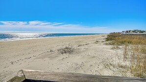 A beach with a wooden boardwalk leading to a building with multiple windows. - Waterfront Gem w/ Balcony in Garden City (Murrells Inlet)