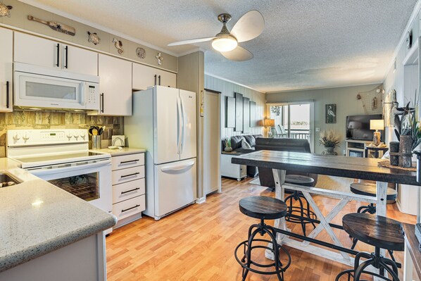 A modern kitchen with white appliances, a wooden floor, and a bar area with stools. - Waterfront Gem w/ Balcony in Garden City (Murrells Inlet)