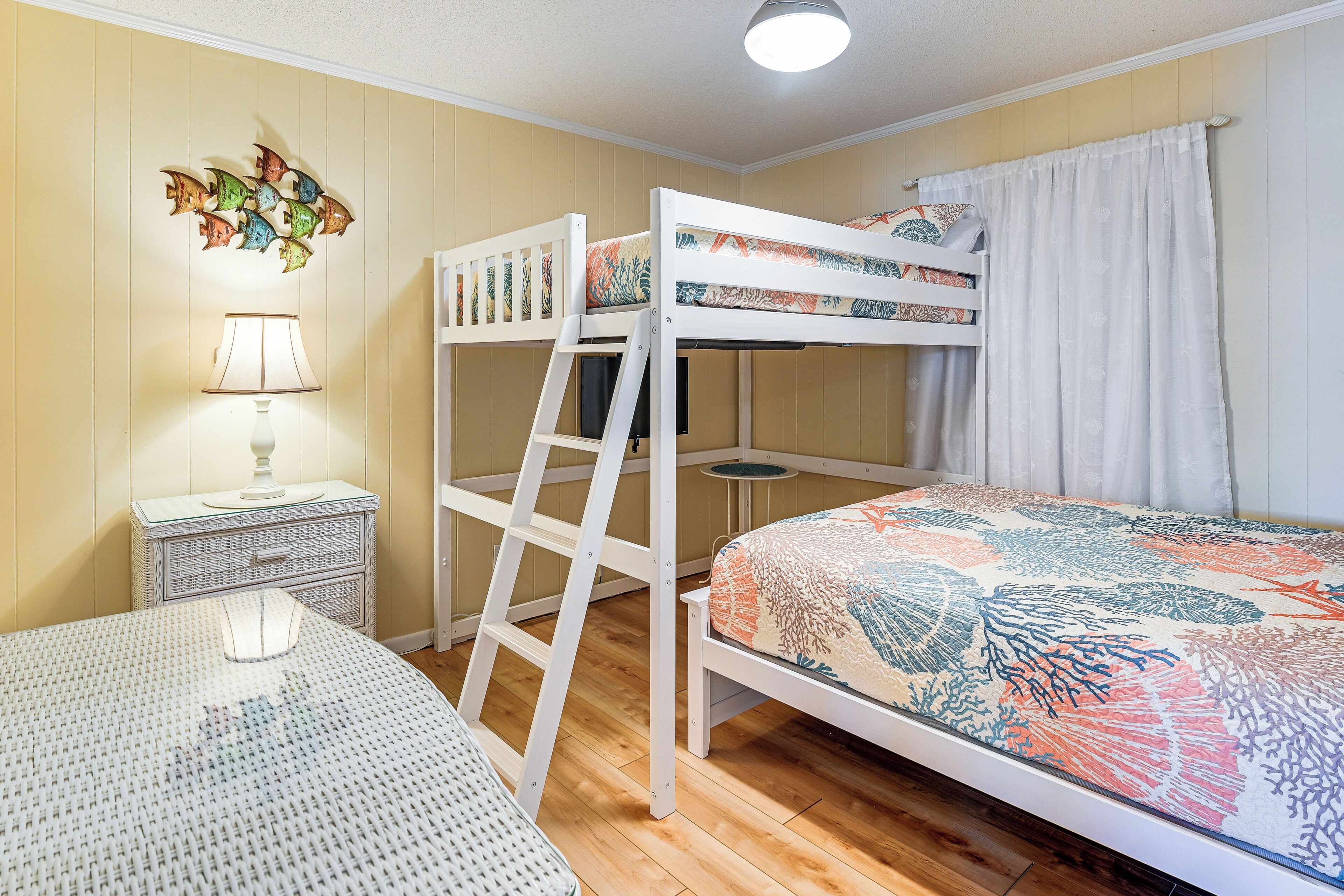 Una cama litera con escalera, una mesita de noche con lámpara, y una mesa redonda con mantel estampado.