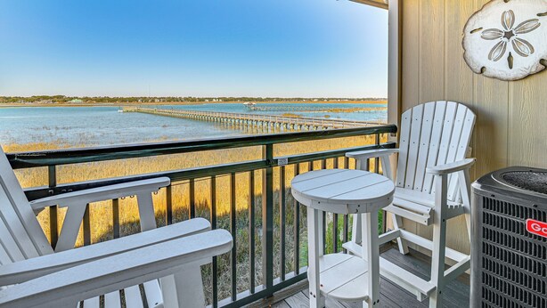 A balcony with white Adirondack chairs and a table, overlooking a beach and pier. - Waterfront Gem w/ Balcony in Garden City (Murrells Inlet)