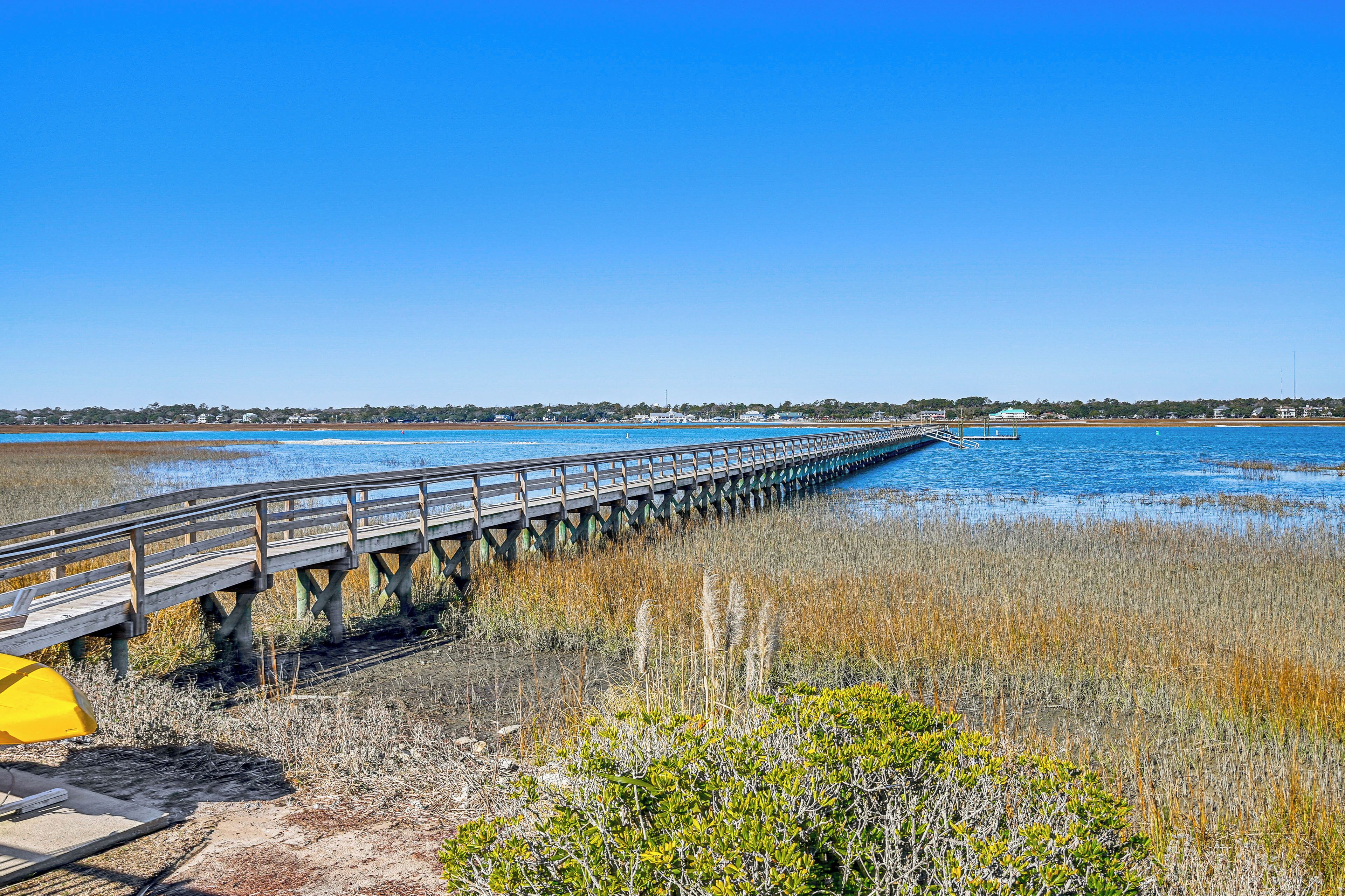A wooden pier extending into a body of water, surrounded by marsh vegetation.