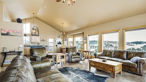 Ein geräumiges Wohnzimmer mit Ledersofas, einem Couchtisch und einem großen Teppich. Mehrere Fenster bieten Blick auf eine verschneite Landschaft.