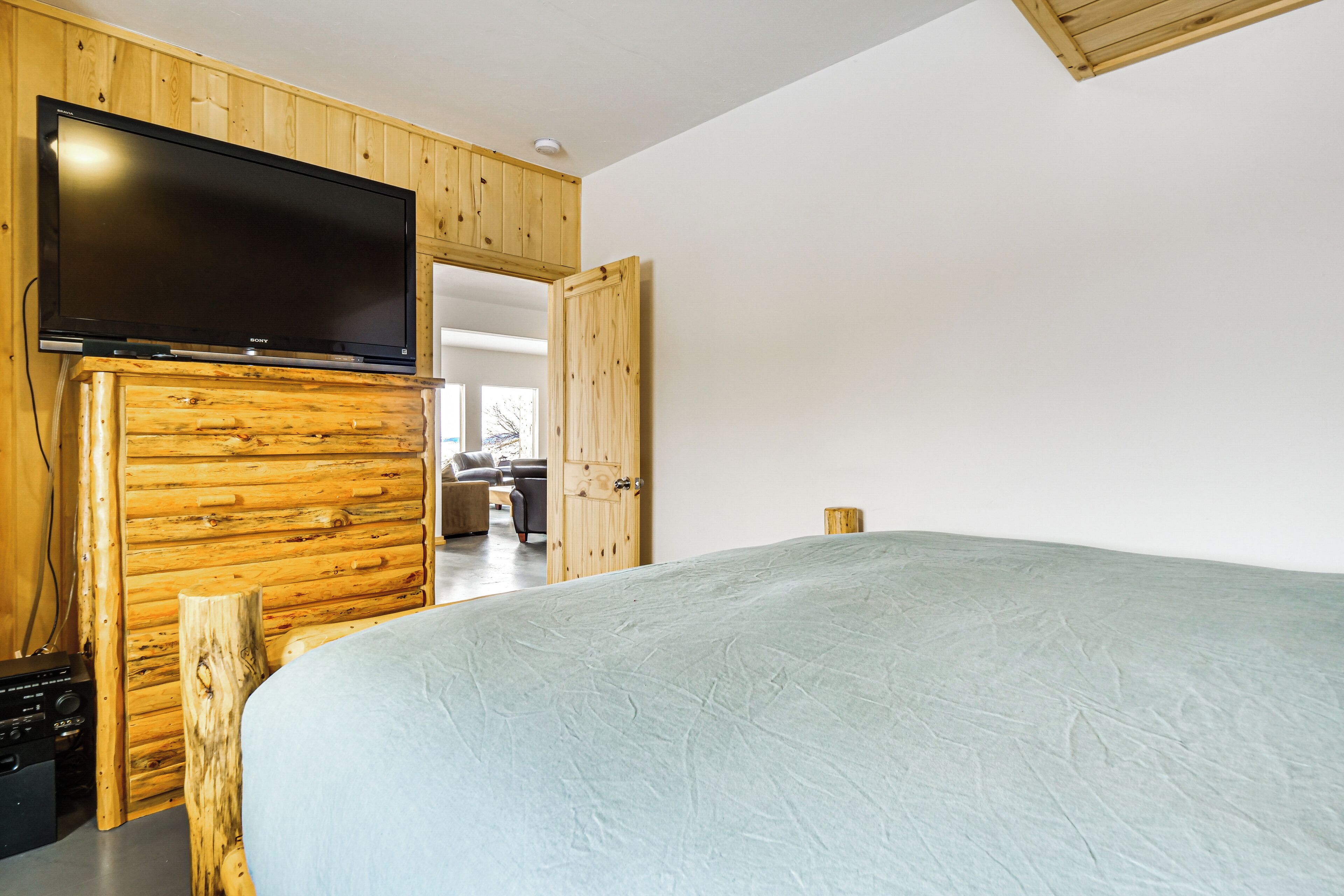 Une chambre à coucher avec un lit, un lambris en bois, un téléviseur à écran plat et une porte en bois donnant sur une autre pièce.