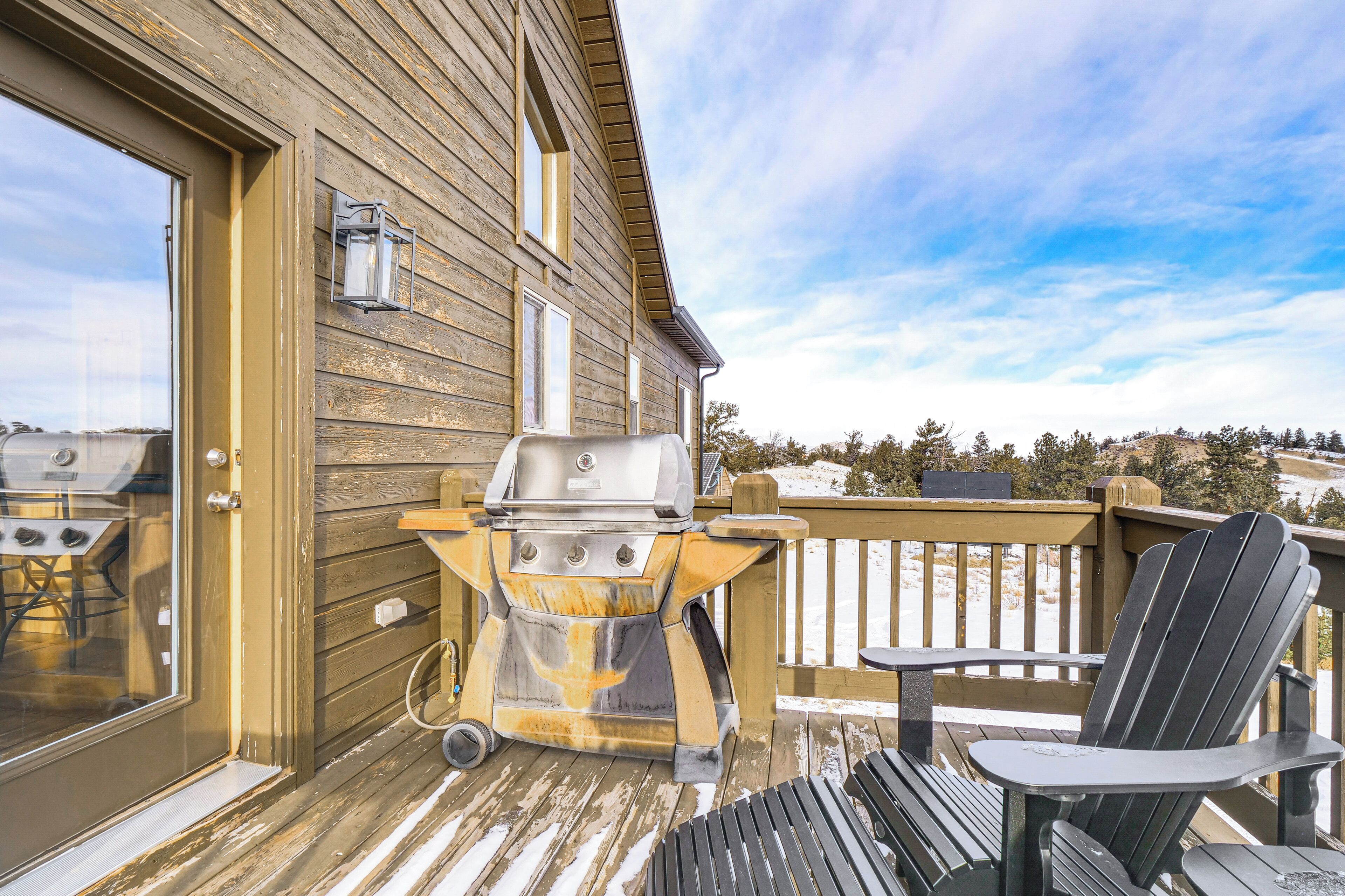 A wooden deck with a grill, a black Adirondack chair, and a glass door leading to a patio area.