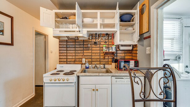 A compact kitchen with a stove, sink, and white cabinets.