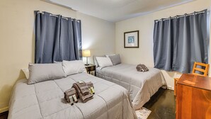 A hotel room with two beds, a desk, a chair, and a lamp.