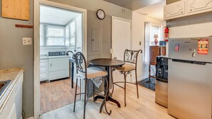 A kitchen with a dining table and chairs, a clock on the wall, and a refrigerator.