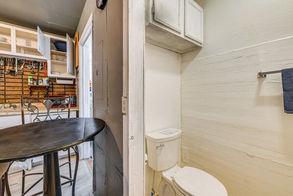 Una cocina compacta con una mesa y sillas, un inodoro blanco y un estante de madera con utensilios de cocina.
