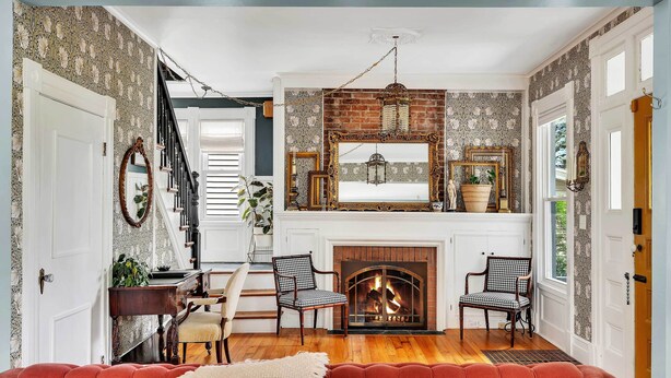 A cozy living room with a fireplace, patterned wallpaper, and a red sofa.