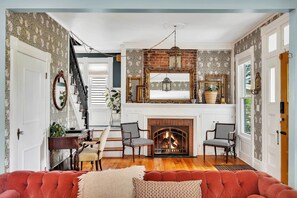 A cozy living room with a fireplace, patterned wallpaper, and a red sofa. - Spacious Home w/ Yard & Patio, 2 Mi to Dtwn Troy (Troy)
