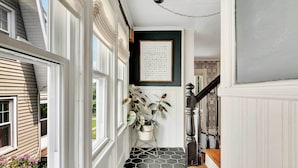 A hallway with a black and white hexagonal tile floor, white walls, and a framed artwork on the wall.