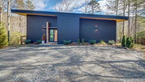 A modern building with a dark exterior, a cross on the front, and a gravel driveway. - Hot Tub + Fire Pit: Modern North Carolina Retreat (Pisgah Forest)