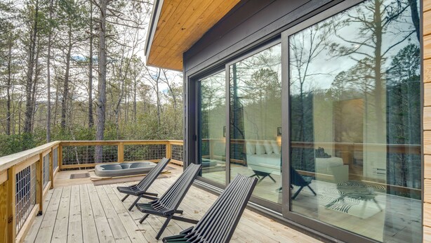 A wooden deck with three lounge chairs, a glass wall, and a view of a forest. - Hot Tub + Fire Pit: Modern North Carolina Retreat (Pisgah Forest)