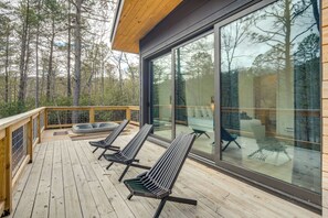 A wooden deck with three lounge chairs, a glass wall, and a view of a forest. - Hot Tub + Fire Pit: Modern North Carolina Retreat (Pisgah Forest)