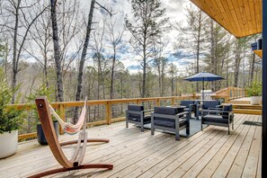 A wooden deck with outdoor furniture, a hammock, and a grill area. - Hot Tub + Fire Pit: Modern North Carolina Retreat (Pisgah Forest)