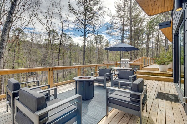 A deck with outdoor furniture and a fire pit, surrounded by trees. - Hot Tub + Fire Pit: Modern North Carolina Retreat (Pisgah Forest)