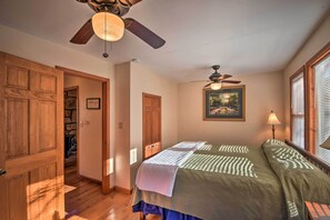 A bedroom with two beds, wooden doors, a ceiling fan, a painting, and a window with blinds. - Twin Pines Hill House - Fire Pit & Mountain View (Ellijay)