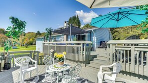 A deck with outdoor furniture, a table with a centerpiece, and a large umbrella providing shade. - Creekside Catskills Retreat: Deck, Bbq, & Firepit (Parksville)