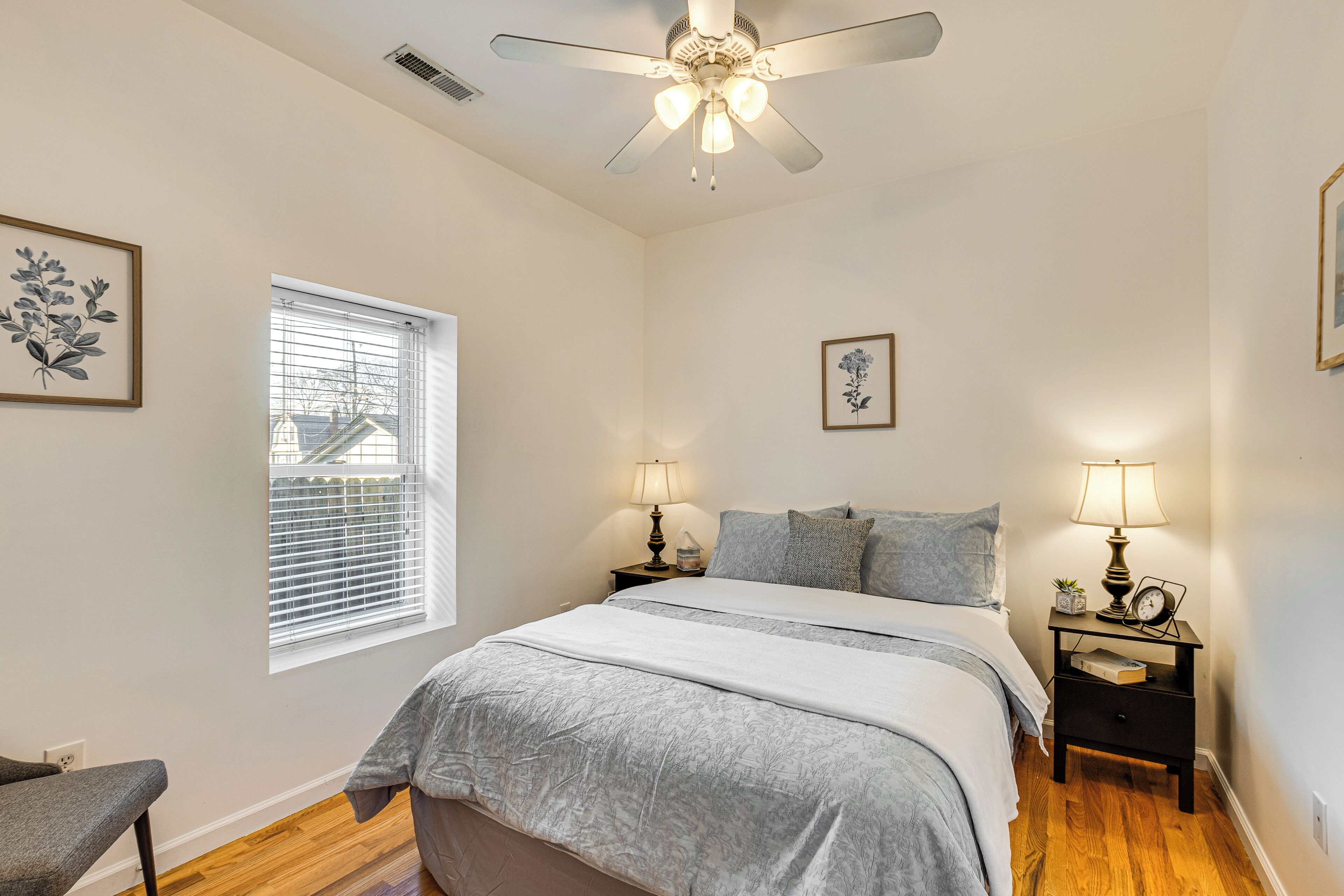 A bedroom with a bed, two bedside tables with lamps, a ceiling fan, and a window with blinds.