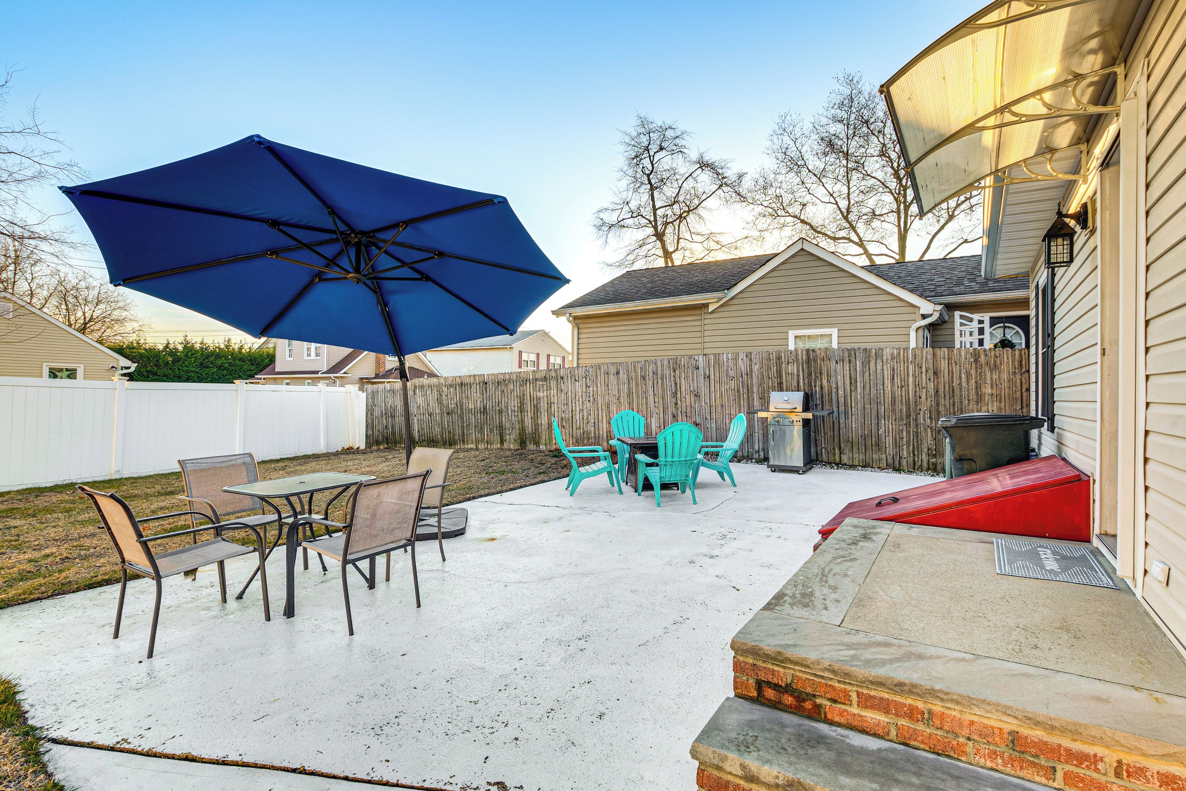 A patio with a table and chairs, a blue umbrella, and a wooden fence.