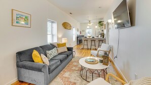 Una sala de estar moderna con un sofá gris, una mesa de centro redonda y una zona de cocina al fondo.