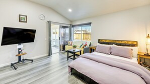 A modern hotel room with a large bed, a flat-screen TV mounted on the wall, a small table, and a window with a view of the outside.
