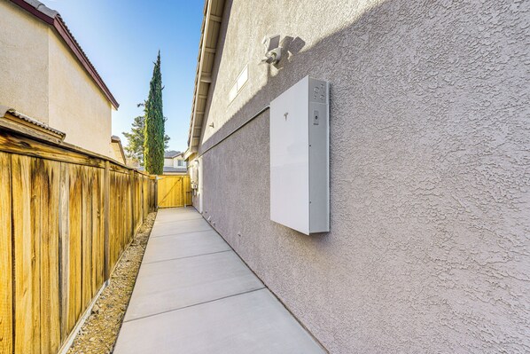 A narrow concrete pathway flanked by a wooden fence and a textured wall with a utility box mounted on it.