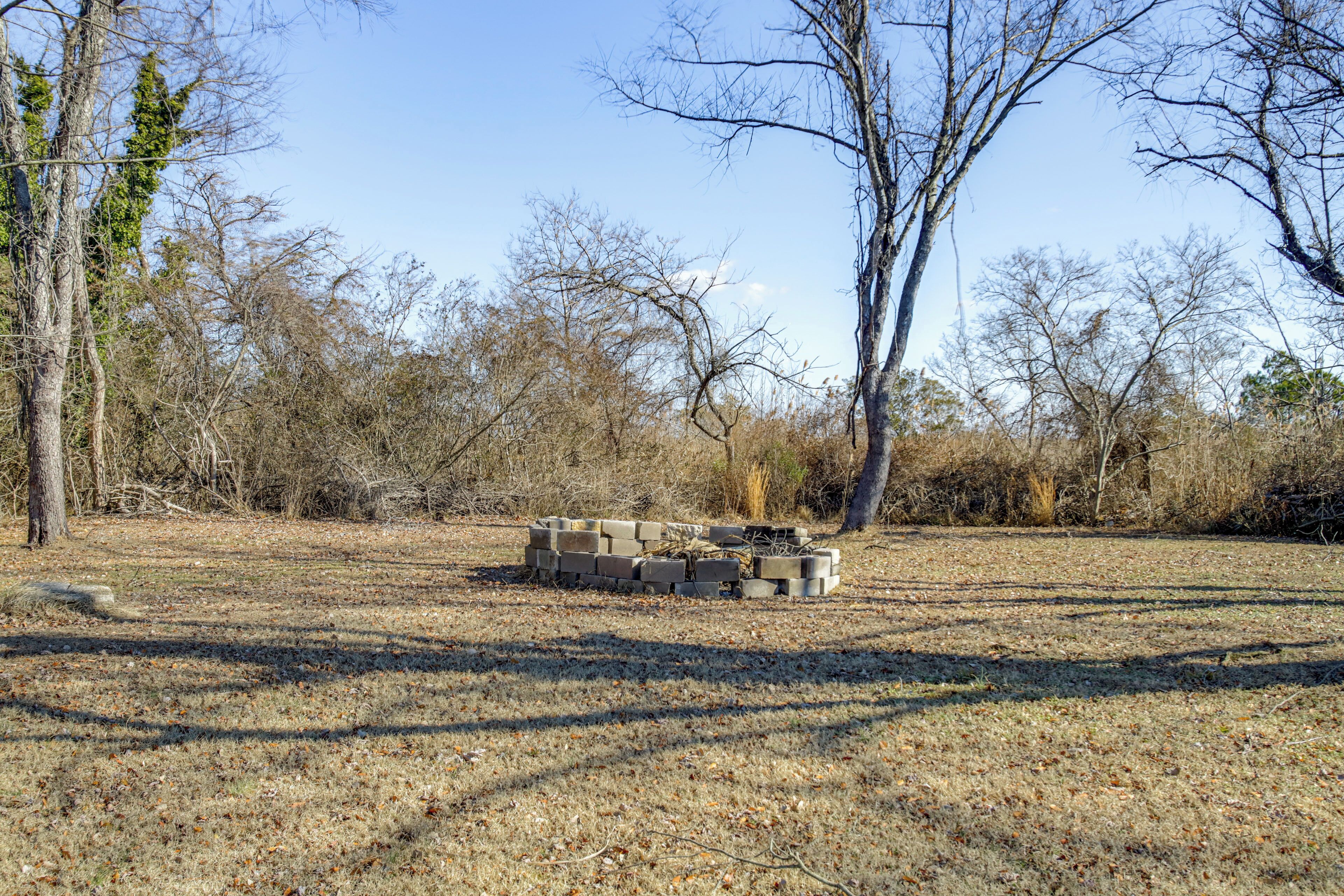 A dry grassy field with a stack of concrete blocks in the center, surrounded by leafless trees.