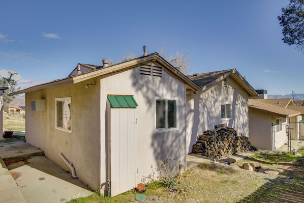 A single-story house with a green awning, a small attached garage, and a stack of firewood outside.