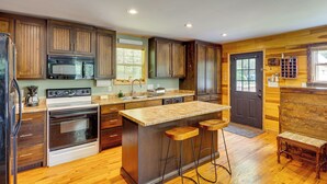 A kitchen with wooden cabinets, a central island with stools, a refrigerator, an oven, and a microwave. - Peaceful Cabin at Lake Logan w/ Spacious Yard! (Ardmore)