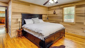 A wooden-paneled bedroom with a bed, a ceiling fan, and a window. - Peaceful Cabin at Lake Logan w/ Spacious Yard! (Ardmore)